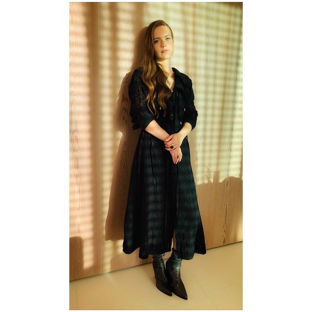 Hera Hilmar in a black dress and black boots.